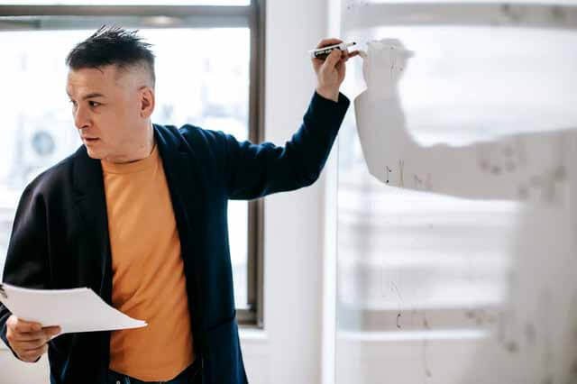 teacher writing on board looking back at students